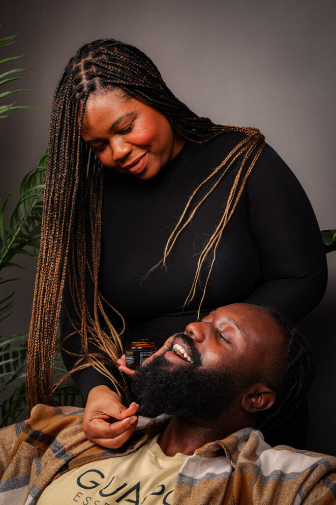 Black woman applying beard oil to smiling Black man (Guapo), co-founder of Guapo Essentials.